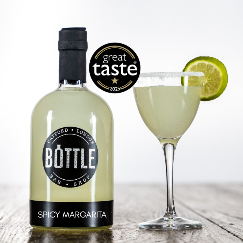 Bottle Spicy Margarita bottle with a glass of margarita and lime wedge on a wooden surface.